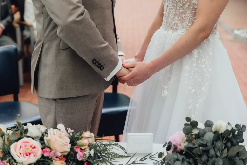 Nahaufnahme auf Hände von Hochzeitspaar während des Ehegelübdes, Dabei schaut die Manschette des Mannes am Ärmel hervor