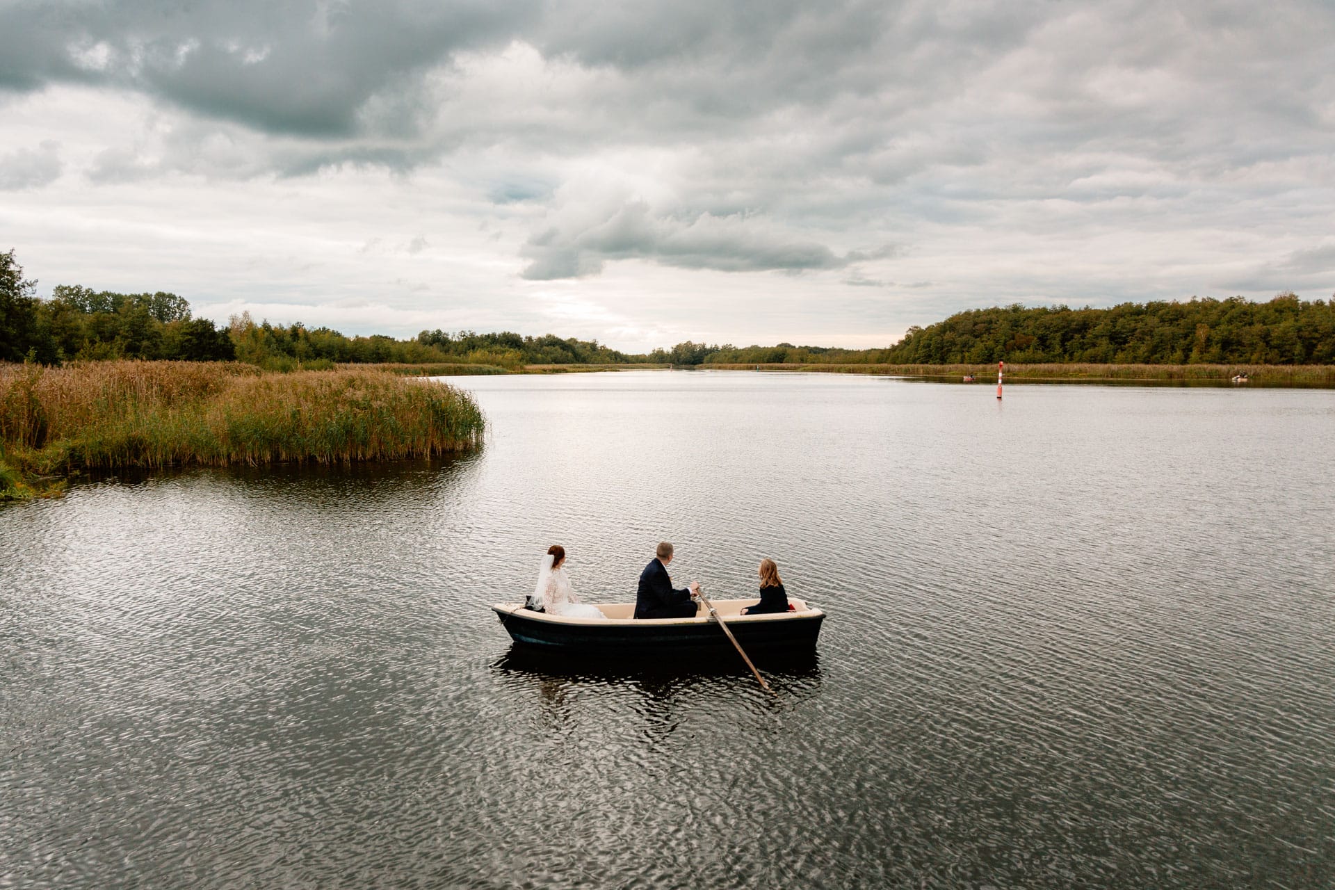 Brautpaar sitzt mit Sohn in einem Boot während des Fotoshootings, Panoramaaufnahme. Hochzeitsreportage